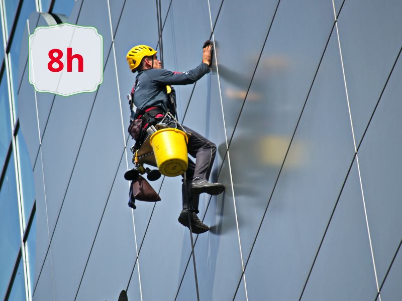 Aggiornamento per addetti ai lavori con sistemi di accesso e posizionamento mediante funi su strutture artificali modulo 1 - AIFOR.IT Window cleaner in safety gear climbs the glass facade, a yellow bucket hanging from his harness; an '8h' label appears in the corner.